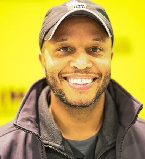 A man wearing a hat and jacket smiling for the camera.