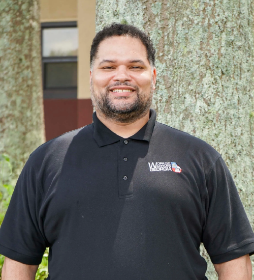 A man in black shirt standing next to tree.